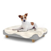 Hund sidder på en lille Topology hundeseng med fåreskind og runde træfødder