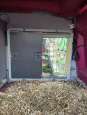 En grå automatisk døråbner monteret inde i en lyserød plastikhønsegård