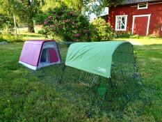 En lyserød hønsegård med tilhørende løbegård, dækket af en skygge, med et smukt rødt hus i baggrunden