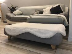 En grå seng med en hvid top af fåreskind og firkantede træfødder