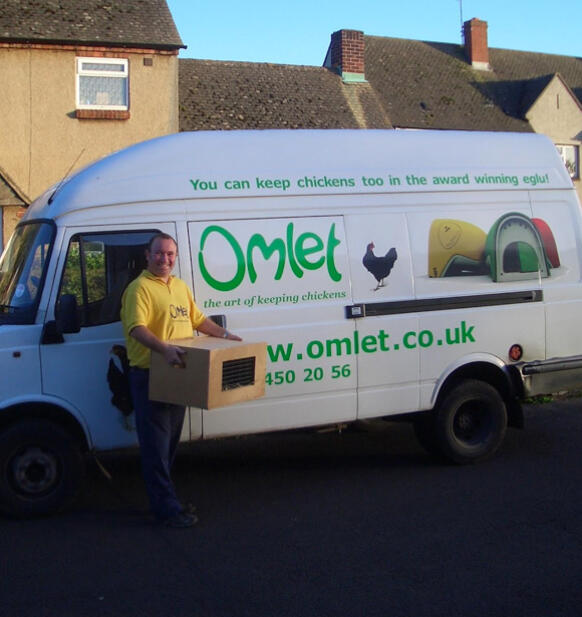 En chauffør ved siden af en varevogn af mærket Omlet med en kasse kyllinger.