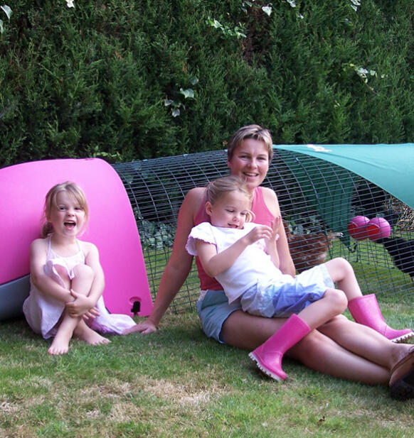 En familie sidder ved siden af en lyserød Eglu hønsegård
