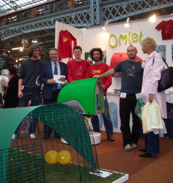 En gruppe mennesker poserer ved en stand med Eglu Cube hønsehus.
