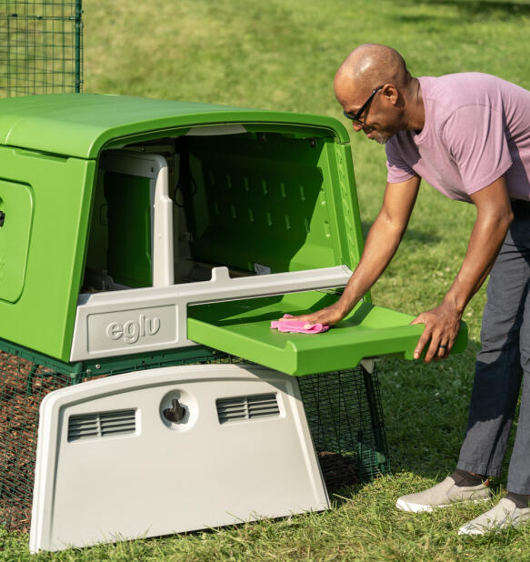 En mand, der renser hønsegårdens Eglu Cube gødningsbakke.