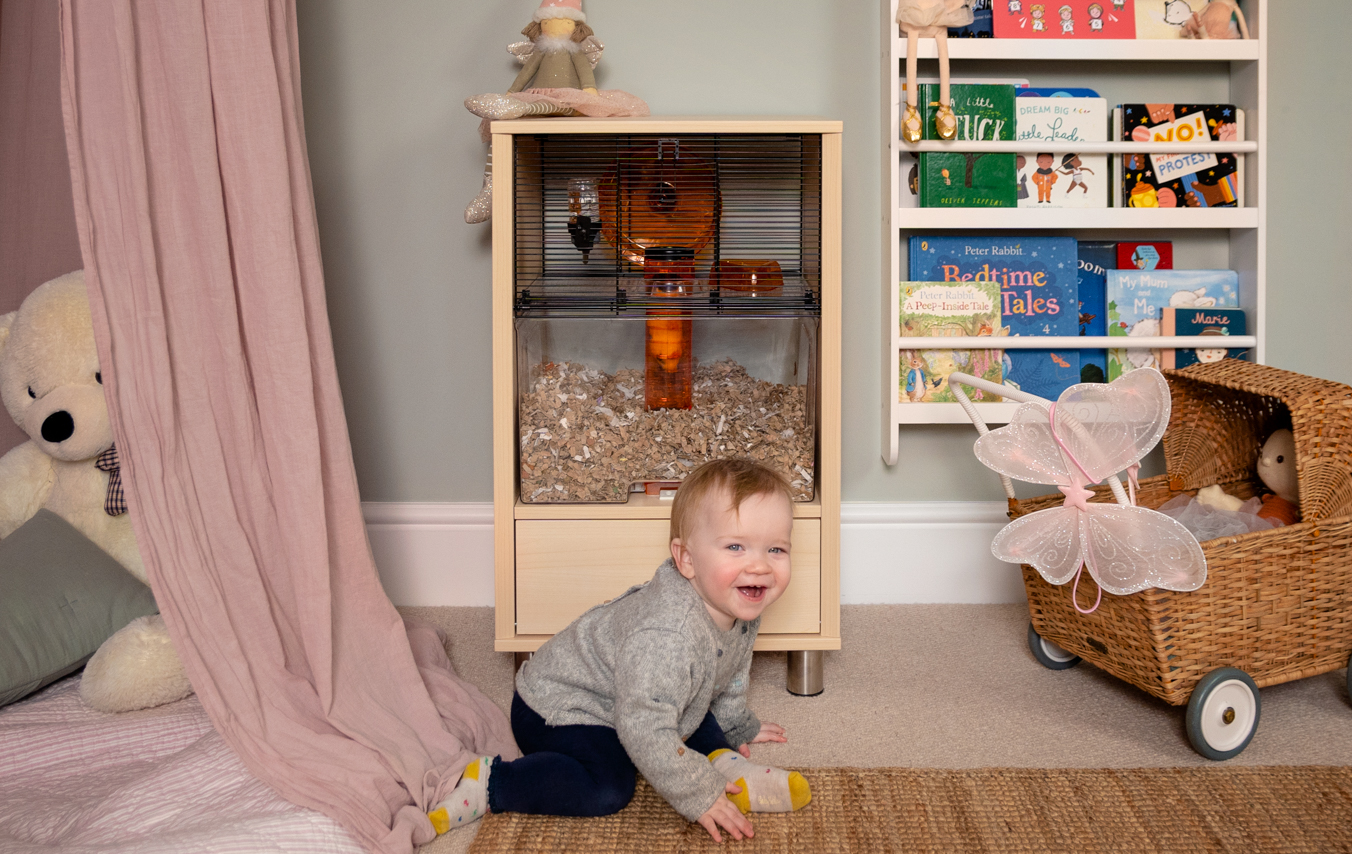 Lille barn, der leger i et soveværelse med et hamsterbur i baggrunden