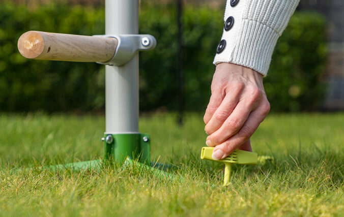 Kvinde sikrer det fritstående hønsetræ med siddepinde til græsplænen med let brugbare skruepløkker
